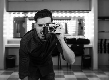 man holding camera bending down in grayscale photography