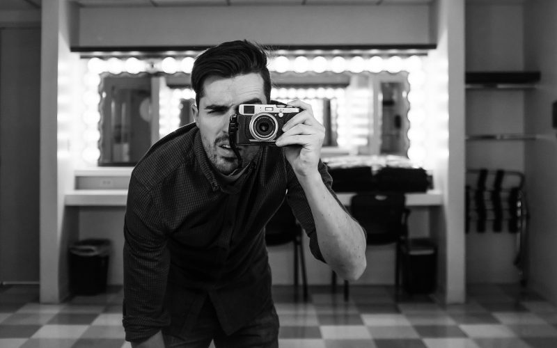 man holding camera bending down in grayscale photography