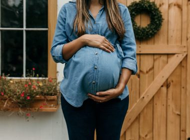 woman in blue denim button up jacket and blue denim jeans standing near brown wooden fence