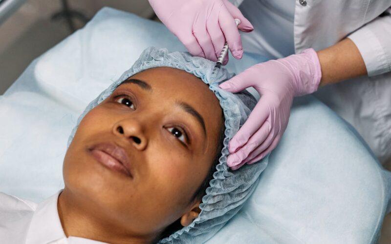Close-up of a cosmetic procedure using injectables on a woman's forehead in a clinic setting.